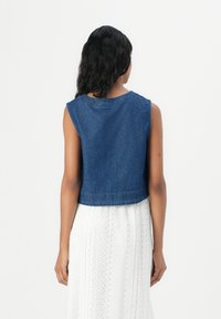 Denim cropped väst i mörkblått med ärmlös design. Avslutade kanter och klassisk halsringning. Matchar med en vit texturerad kjol nedanför.