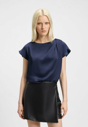 Navy satin blouse with short sleeves and a draped design, paired with a black leather mini skirt featuring a smooth texture and clean lines.