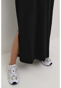 Mustapuku, jossa on sivuaukko, valmistettu sileästä kankaasta. Yhdistetty harmaisiin ja valkoisiin urheilukenkiin, joissa on verkkoyksityiskohtia ja nauhoja.