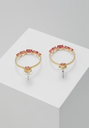 Złote kolczyki koła z różowymi owalnymi kamieniami u góry oraz małymi przezroczystymi kamieniami na obręczy, prezentowane na białej powierzchni.