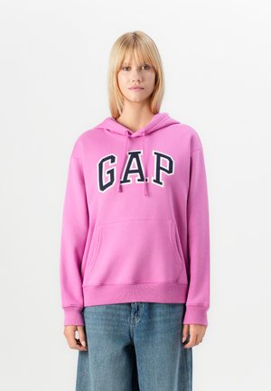 Rosa hettegenser med "GAP" i fet svart skrift. Har en frontlomme, snøring i hetten og ribbestrikkede mansjetter. Mykt materiale og uformell design.