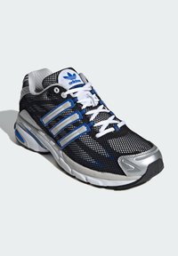 Scarpa da corsa nera in mesh con accenti argento e blu, caratterizzata da sovrapposizioni a tre strisce, una linguetta imbottita e una suola testurizzata.