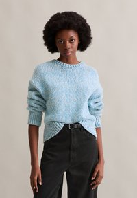 Teksturowany niebieski sweter dzianinowy z okrągłym dekoltem i prążkowanymi mankietami, w połączeniu z czarnymi spodniami z wysokim stanem i czarnym paskiem.