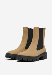 Botas Chelsea de cuero marrón claro con un panel lateral elástico negro, punta rectangular y suela de goma negra gruesa con un patrón de tracción texturizado.