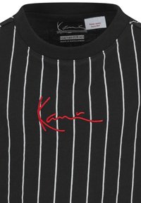 Svart t-shirt med vita vertikala ränder och en röd broderad logotyp på bröstet. Har rund halsringning och etikett som anger brand säkerhet.