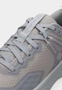 Κοντινό πλάνο ενός γκρι αθλητικού παπουτσιού με λεπτομερείς κορδόνια, αναπνεύσιμο επάνω μέρος από δίχτυ και λογότυπο της Columbia στη γλώσσα και στο πλάι.