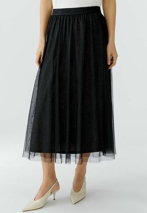 Zwarte glitter midi-rok met transparante overlay, elastische tailleband, gedragen met witte slingback hakken met puntige neus, torso en benen zichtbaar.