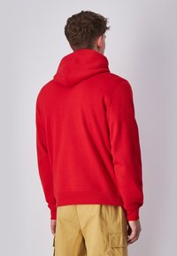 Rode hoodie met een grote capuchon, lange mouwen en ribgebreide manchetten en zoom. Gemaakt van zacht materiaal, heeft het een relaxte pasvorm en een gladde textuur.