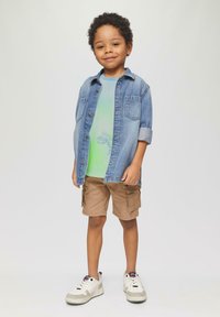 Denim särk rohelise gradientiga T-särgi peal, khaki cargo lühikesed püksid ja valged tennisetossud hallide aktsentidega. Lihtne disain, vabaaja sobivus.