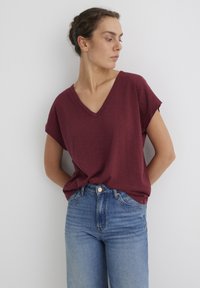 Burgundy V-neck T-shirt made of soft fabric, featuring short sleeves and a relaxed fit, paired with high-waisted blue jeans.