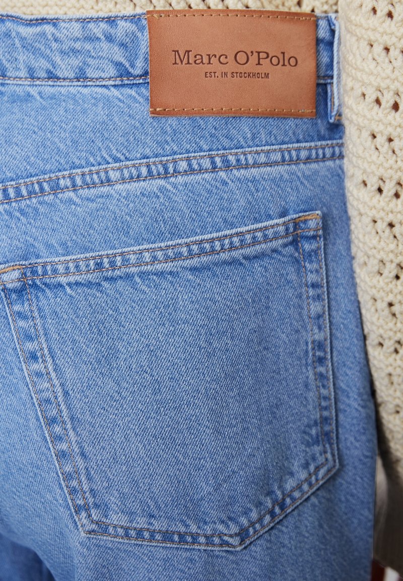 Světle modré džínové kalhoty s viditelnou zadní kapsou. Na pasu je přišitá hnědá kožená nášivka s nápisem "Marc O'Polo, EST. IN STOCKHOLM".