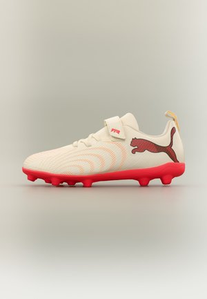 Λευκό και κόκκινο ποδοσφαιρικό παπούτσι Puma με υφασμένη σχεδίαση, κόκκινες τάπες στη σόλα, βέλκρο λουράκι και λογότυπο Puma στο πλάι σε ουδέτερο φόντο.