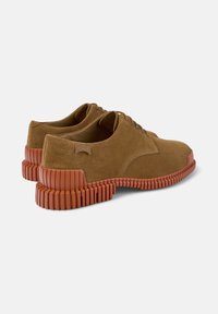 Scarpe in suede marrone con suole in gomma, caratterizzate da un design spesso e scanalato e lacci, viste da dietro e di lato.