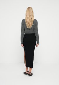 Suéter gris de manga larga combinado con una falda midi negra de canalé con una abertura lateral. Zapatos de tacón negro con correas en el tobillo.