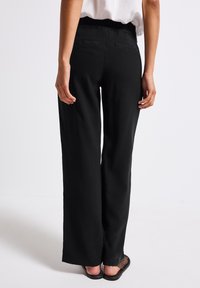 Černé kalhoty s širokými nohavicemi a elastickým pasem, které mají dvě zadní kapsy a hladký povrch, v kombinaci se jednoduchými sandály.