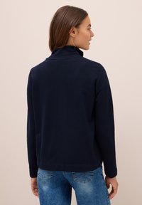 Pullover blu navy con colletto alto, maniche lunghe e orlo dritto. Realizzato in morbido tessuto di cotone, presenta cuciture minime e un design semplice.