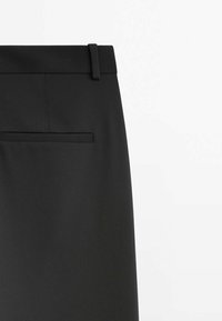 Jupe crayon noire à texture douce, dotée d'une ceinture, d'une poche arrière unique et de détails discrets de couture.