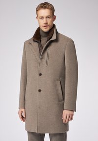 Cappotto da uomo in misto lana beige, con colletto foderato in pelliccia marrone, chiusura con due bottoni e tasca laterale, dal taglio aderente.