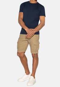 T-shirt à manches courtes bleu marine associé à un short en toile kaki avec poches latérales, cordons de serrage réglables et baskets blanches.