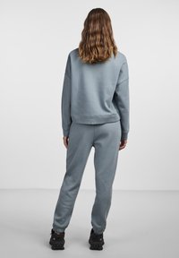 Grå hettegenser og joggebukse i myk stoff, med avslappet passform og ribbestrikkede mansjetter, sammen med svarte teksturerte sko.