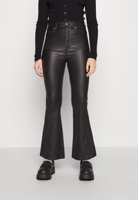 Calças flare de imitação de couro pretas com cintura alta, textura suave e costuras laterais discretas. Combinadas com sapatos pretos com padrão.