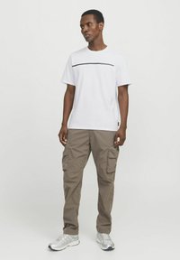 Hvit t-skjorte med en svart horisontal stripe, kombinert med beige cargo-bukser med sidelommer, og grå joggesko.
