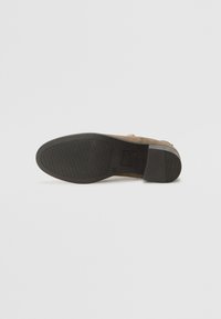 Bottine en suede marron clair avec une semelle en caoutchouc noir. La semelle présente un motif de grip texturé et un petit talon. Design minimaliste sans embellissements visibles.