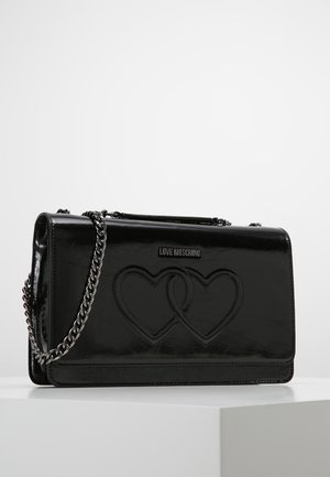 Sac à bandoulière Moschino noir avec finition brillante, deux cœurs en relief et bandoulière chaîne argentée sur une surface blanche.