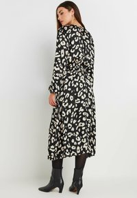 Vestido negro con estampado de leopardo crema, mangas largas, cintura ceñida y falda fluida. Lleva puestas botas negras hasta el tobillo.