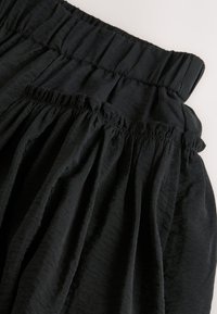 Svart kjol med elastisk midjeresår och veck; texturerat tyg med lätt glans; mjukt, lätt material.