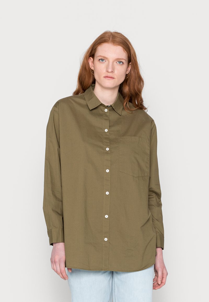 Camisa abotoada verde-oliva feita de algodão, com colarinho, mangas longas, um bolso no peito e botões brancos na parte da frente.