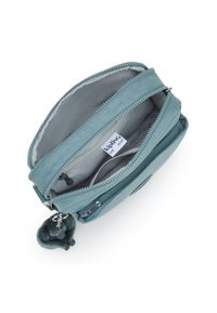Pochette con zip color turchese con due scomparti, realizzata in tessuto. L'interno presenta un'etichetta ed è foderato in grigio chiaro. Include un portachiavi morbido.