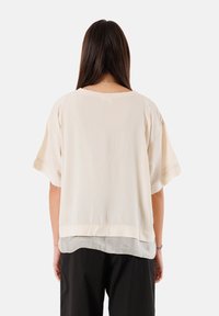 Blusa leggera color crema, con maniche corte, caratterizzata da un orlo a strati e una texture morbida. Adatta per un look casual.