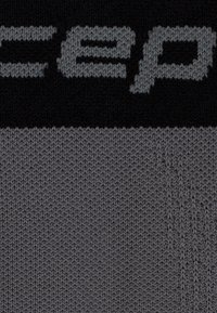 Tessuto lavorato a maglia in nero e grigio scuro, con un logo di colore grigio chiaro ben visibile. La texture è uniforme, con un motivo di maglia di media densità.