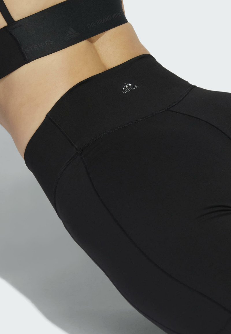 Leggings noirs taille haute en tissu extensible, dotés de coutures plates et d'un petit logo. Texture lisse avec une coupe ajustée.
