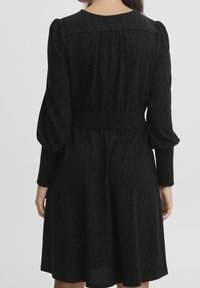 Czarna sukienka z długimi, bufkami i dopasowaną talią. Wykonana z teksturowanej tkaniny, posiada rozkloszowaną spódnicę i okrągły dekolt.