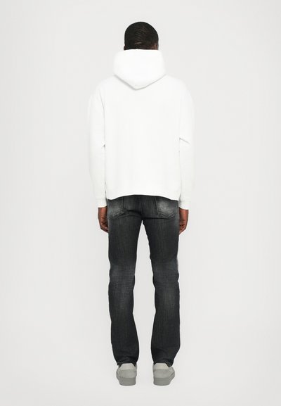 White hooded sweatshirt paired with dark grey jeans and light grey sneakers, view shows back of the outfit, emphasizing fit and color contrast.