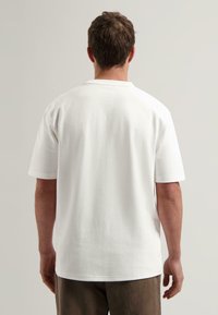 Fehér pamut póló rövid ujjakkal, kerek nyakkivágással, sima textúrával és laza fazonnal. Egyszerű és minimalista design.