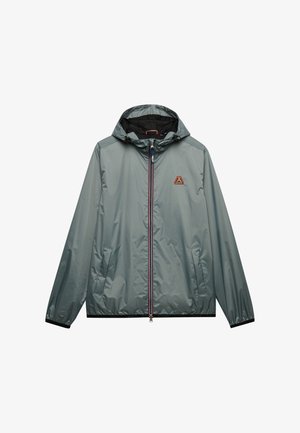 Lichtgrijs windjack met capuchon, voorrits, twee zijzakken, elastische manchetten en een klein kleurrijk logo op de borst.