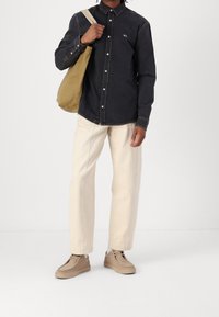 Mörk denimskjorta med knappar, krämfärgade byxor och beiga sneakers. Accessoarer inkluderar en brun tygväska. Enkel design och neutral färgpalett.