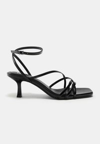 Sandale noire à brides avec bout carré, petit talon fin et bride de cheville ajustable avec boucle, vue de profil sur fond blanc.
