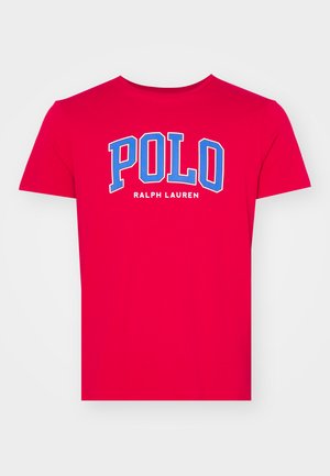 Rød bomull T-skjorte med rund hals og korte ermer. Framsiden viser "POLO" med store blå bokstaver over "RALPH LAUREN" i mindre skrift.