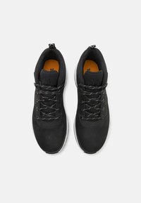 Black athletic shoes with a suede and mesh upper, reflective laces, and a contrasting orange insole. White rubber outsole, low-cut design.