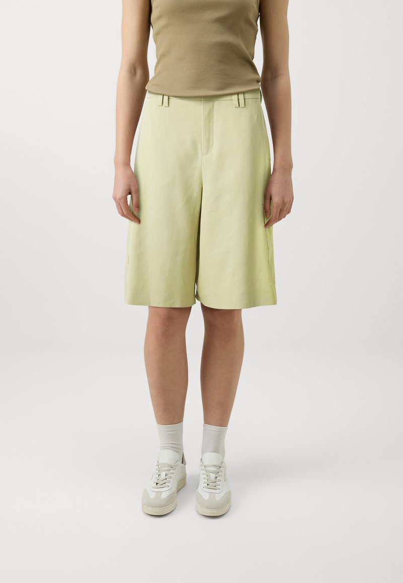 Lys grønne lin shorts med en afslappet pasform, der har sidelommer, plisseret front og en glat overflade. Kombinationen med hvide sneakers og sokker.