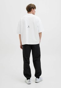 T-shirt en coton blanc oversize à manches courtes, avec un petit logo noir au dos, assortie à un pantalon noir ample et des baskets blanches.