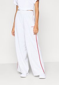 Ανοιχτό γκρι φαρδύ παντελόνι φόρμας με κόκκινες πλευρικές ρίγες και ελαστική μέση. Το λογότυπο "adidas" είναι κεντημένο με κόκκινο στο αριστερό μέρος.