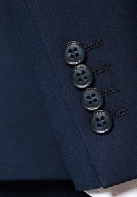 Morska niebieska rękaw kurtki z czterema czarnymi guzikami o gładkiej fakturze, z wyraźnym przeszyciem i subtelnym brandingiem na guzikach.