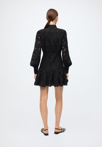 Black lace dress featuring a fitted bodice, puffed long sleeves, a flared skirt, and a tiered hem. Detailed with floral patterns.