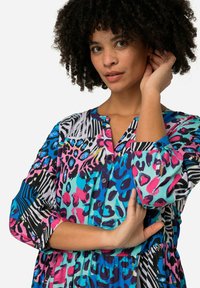 Vestido de botones colorido que presenta una mezcla de estampados animales en rosa, azul y negro sobre un fondo turquesa claro. Tejido fluido con cintura fruncida.