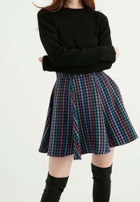 Černý žebrovaný top s dlouhým rukávem spárovaný s rozevlátou mini sukni s vícebarevným vzorem houndstooth v modré, červené, zelené a bílé barvě.